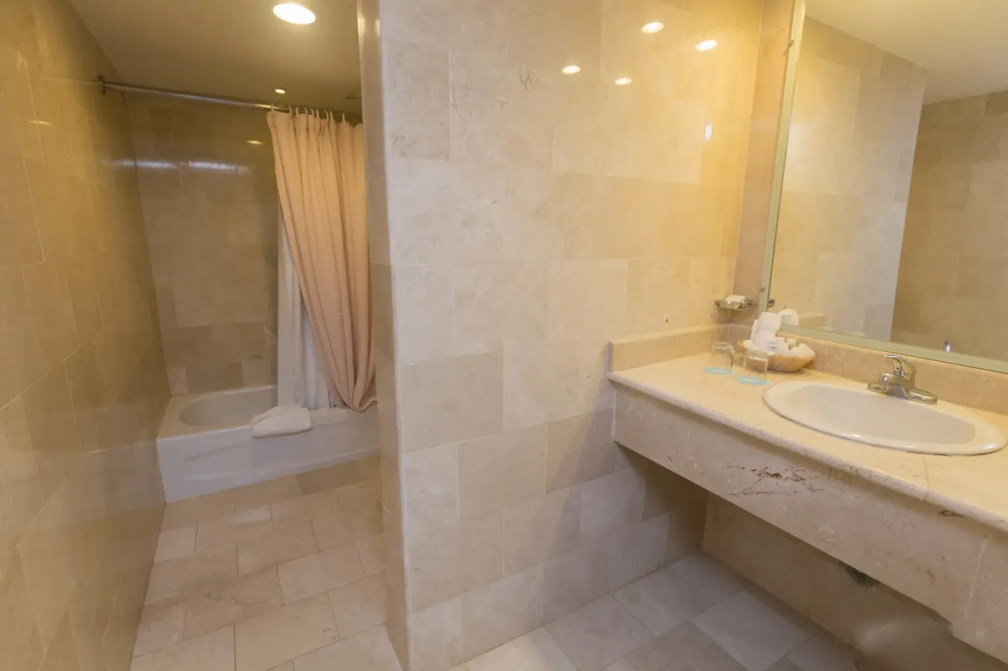 Beige tiled bathroom with vanity and curtained tub at VH Gran Ventana Beach Resort.