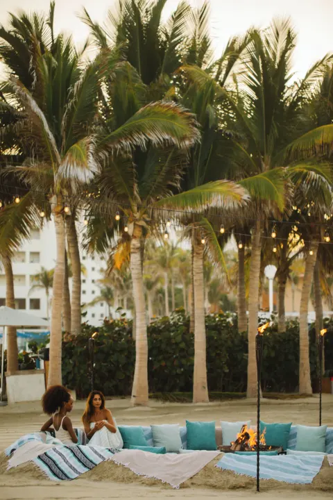 Beach fire lounge with pillows beneath palms at Viceroy Los Cabos.
