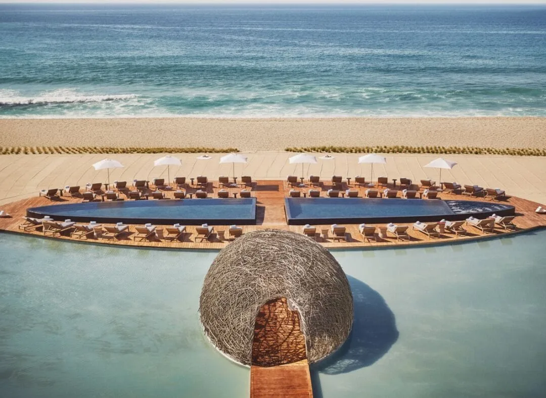 Beachfront pools, lounge chairs and a woven pavilion by the ocean at Viceroy Los Cabos.