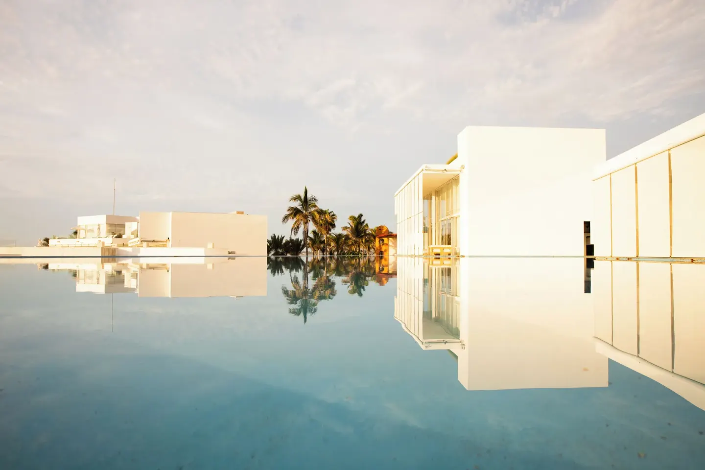 Reflecting pools mirror white resort buildings and palms at Viceroy Los Cabos.