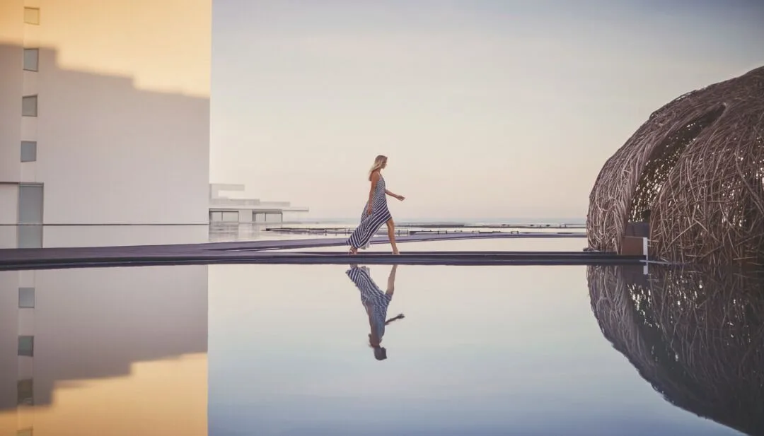 A woman walks beside reflective pools and woven architecture at Viceroy Los Cabos.
