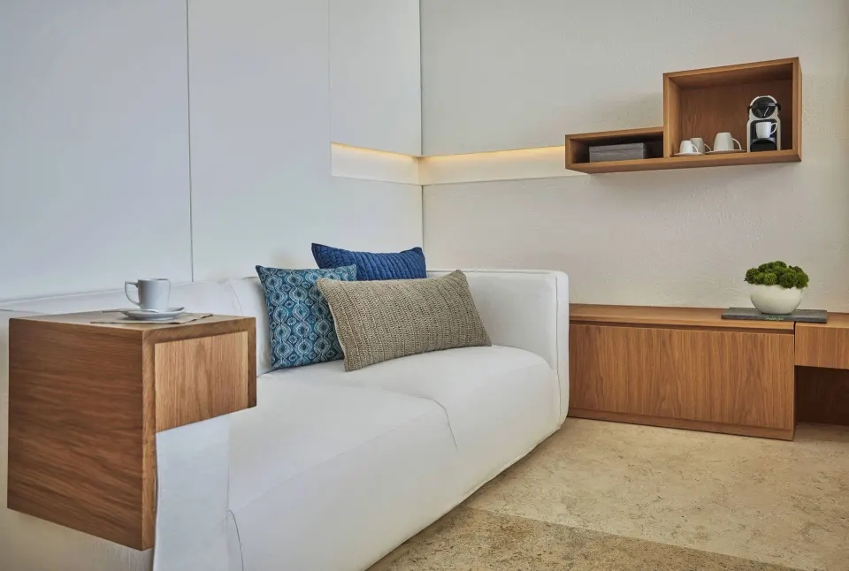 Ocean View room sitting area with white sofa, wood shelving, and coffee setup at Viceroy Los Cabos.