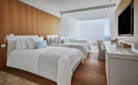 Ocean View room with two beds, wood wall panels, desk, TV, and balcony at Viceroy Los Cabos.