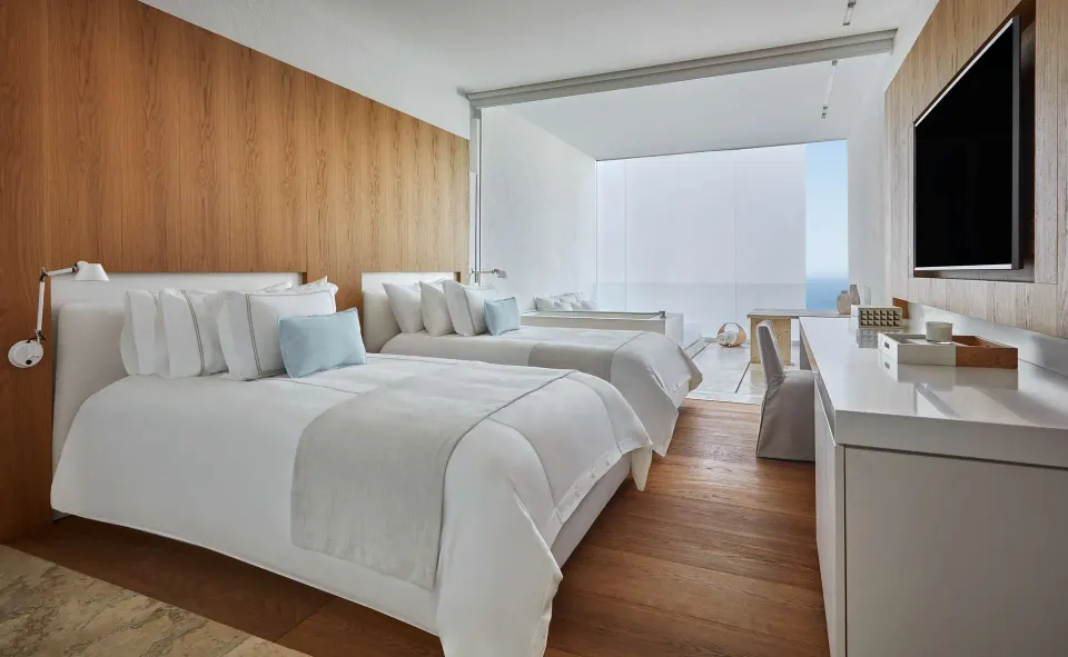 Ocean View room with two beds, wood wall panels, desk, TV, and balcony at Viceroy Los Cabos.
