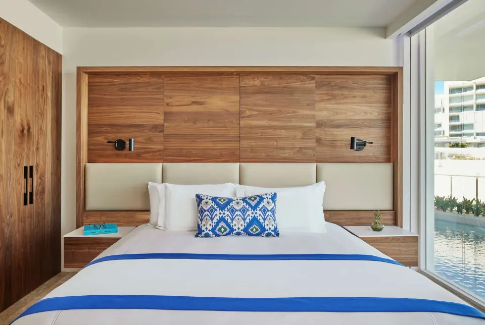 King bedroom with wood headboard and lagoon-facing glass at Viceroy Los Cabos.