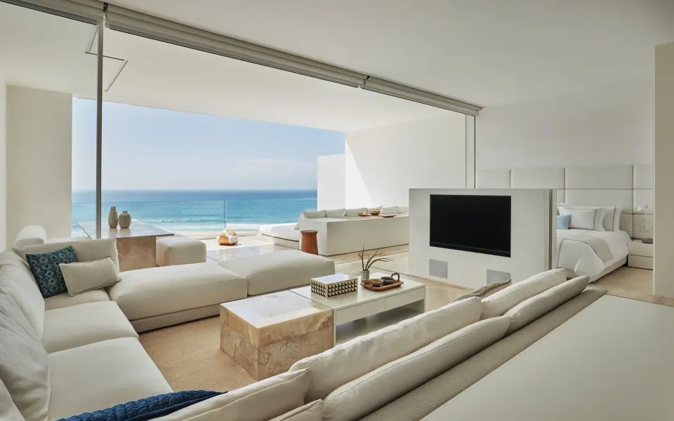 Ocean-view suite living room with sectional sofa, terrace, and king bed at Viceroy Los Cabos.