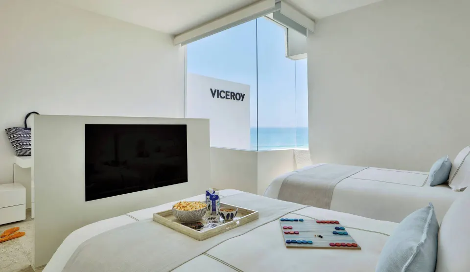 Twin-bed room with TV partition and ocean-facing window at Viceroy Los Cabos.
