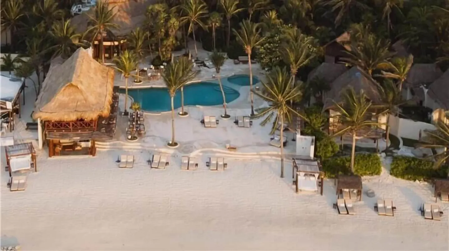 Aerial view of the beachfront pool, palapa structures, and lounge chairs at Viceroy Riviera Maya.