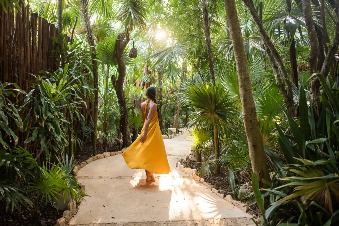 A guest in a yellow dress walks along a lush garden path at Viceroy Riviera Maya.
