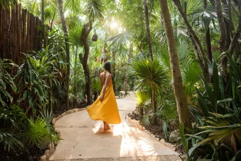 A guest in a yellow dress walks along a lush garden path at Viceroy Riviera Maya.