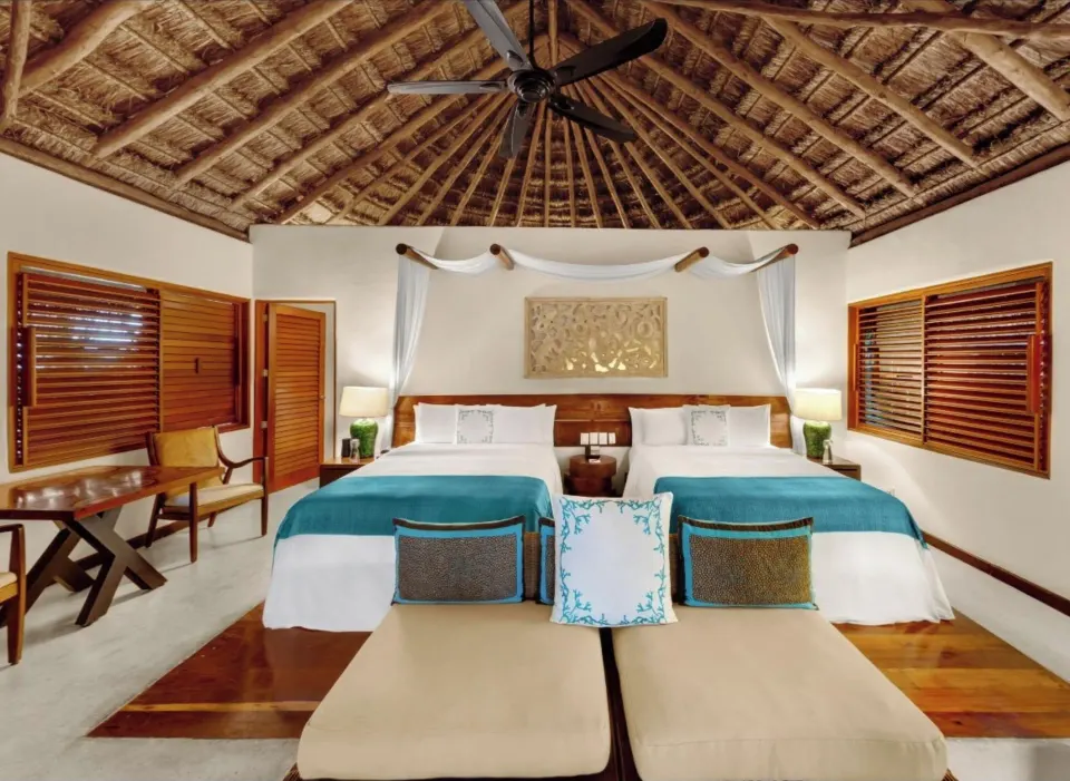 Luxury villa bedroom with two beds and a thatched ceiling at Viceroy Riviera Maya.