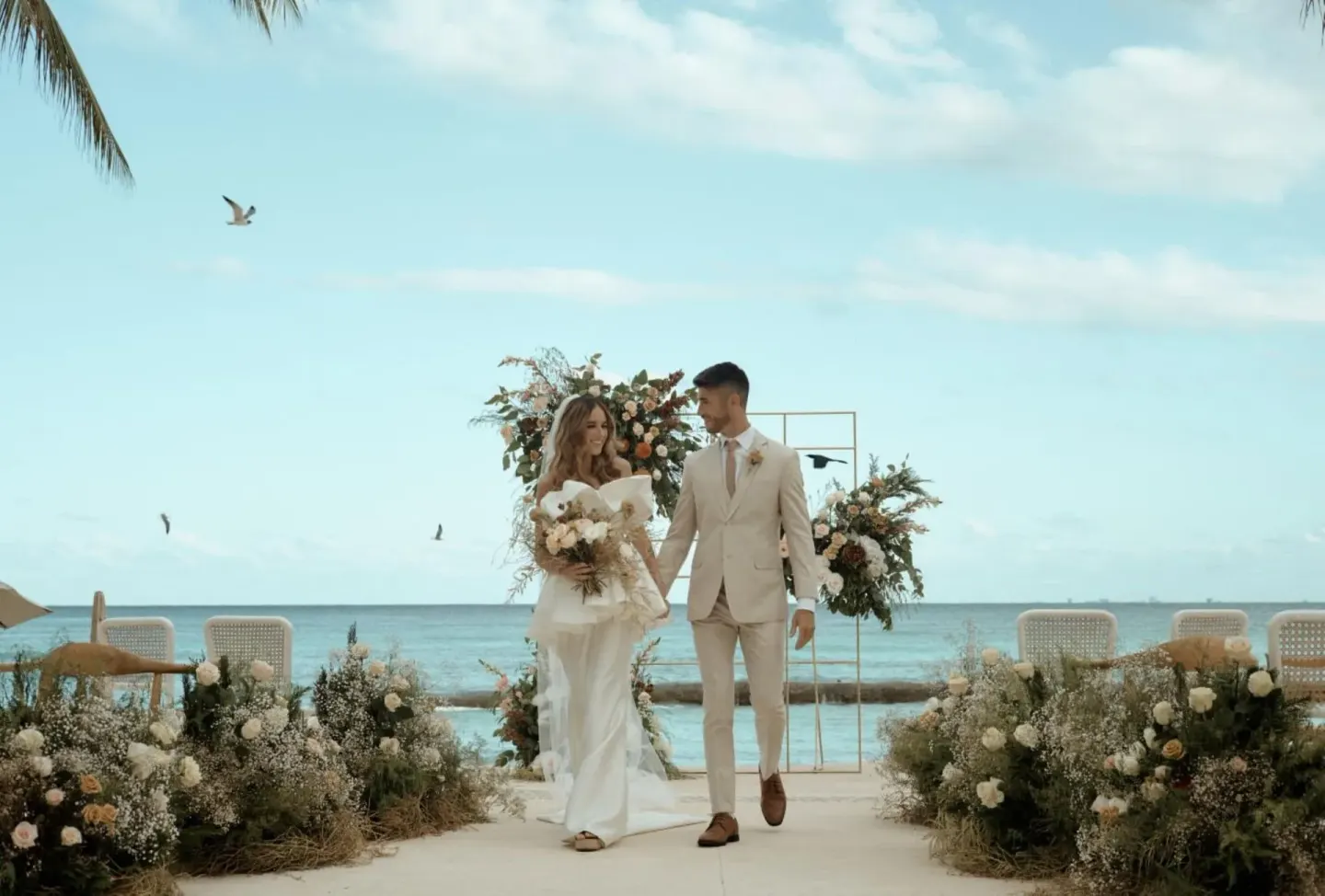 Bride and groom walking through a seaside ceremony setup at Viceroy Riviera Maya.