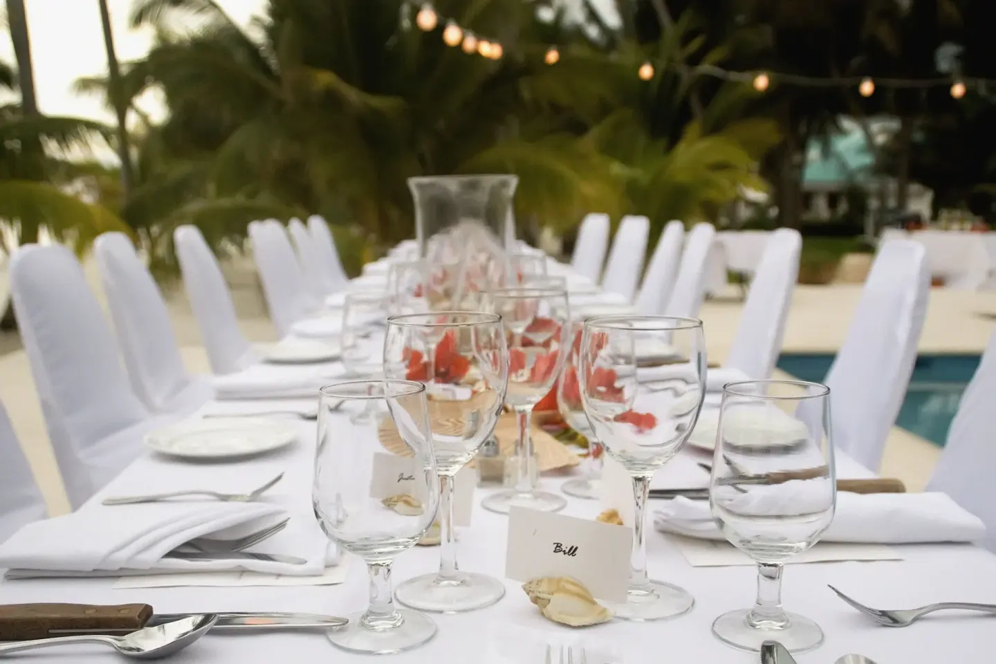 Long outdoor event table set with glassware by the pool at Victoria House Resort & Spa.