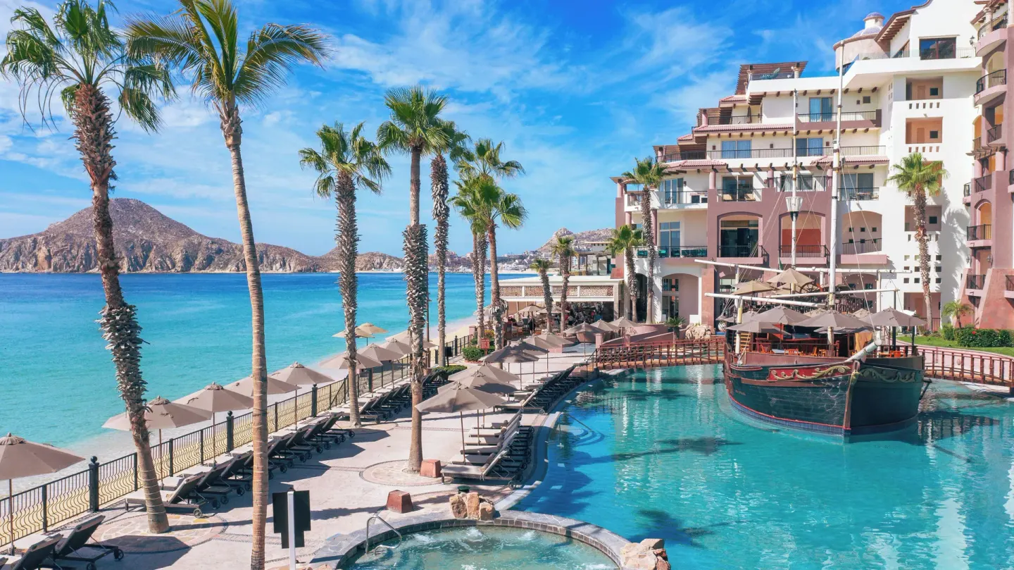 Elevated view of pool, palms, beach, and resort building at Villa del Arco Beach Resort & Spa Cabo San Lucas.
