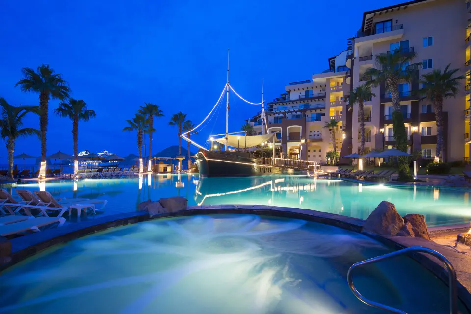 Illuminated pool and ship feature at Villa del Arco Beach Resort & Spa Cabo San Lucas at dusk.
