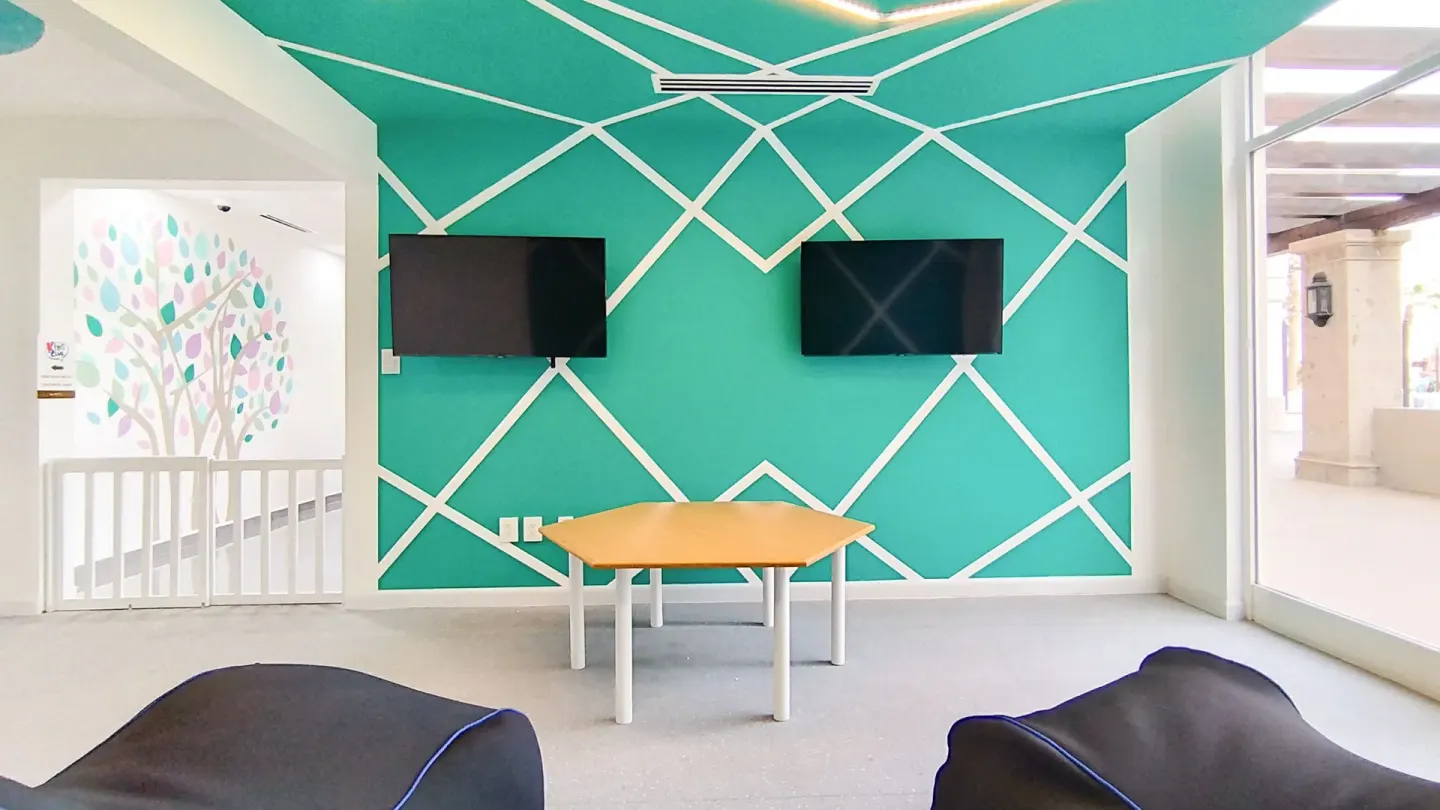 Kids lounge at Villa del Arco Beach Resort & Spa Cabo San Lucas with two wall-mounted screens and a teal accent wall.