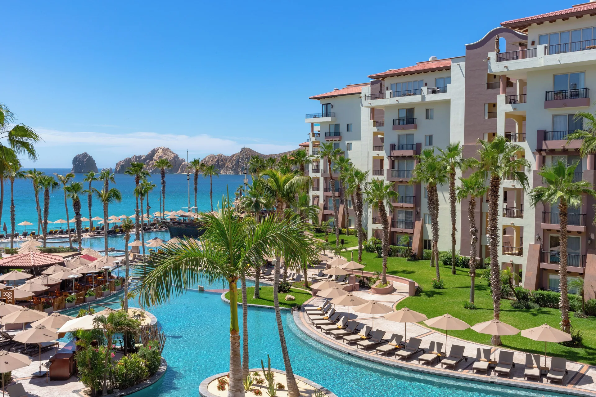 Pool courtyard, palms, and oceanfront buildings at Villa del Arco Beach Resort & Spa Cabo San Lucas.