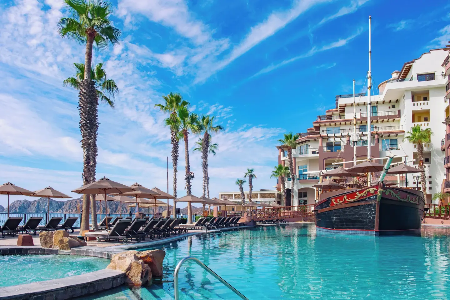 Pool steps, palms, loungers, and ship feature at Villa del Arco Beach Resort & Spa Cabo San Lucas.