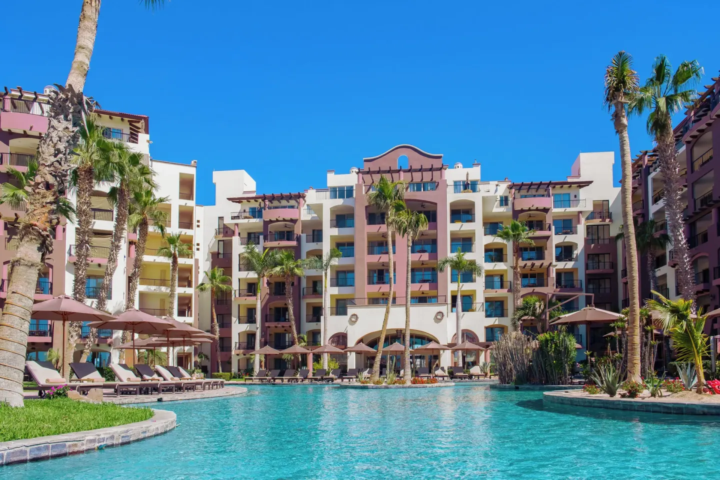 Poolside resort building and palm-lined deck at Villa del Arco Beach Resort & Spa Cabo San Lucas.