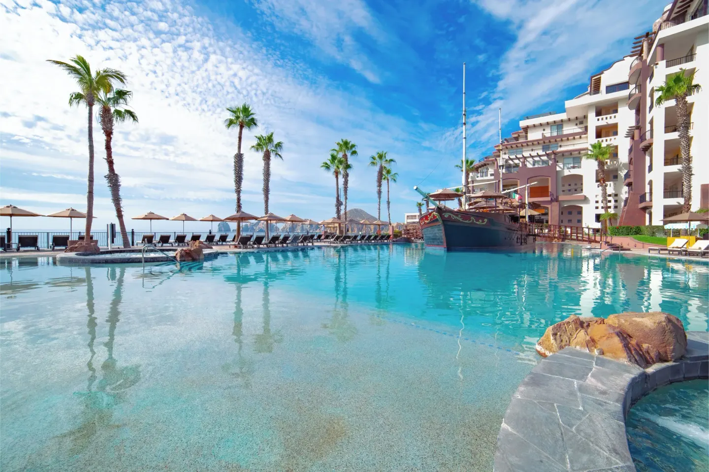 Resort pool with ship feature and palm trees at Villa del Arco Beach Resort & Spa Cabo San Lucas.