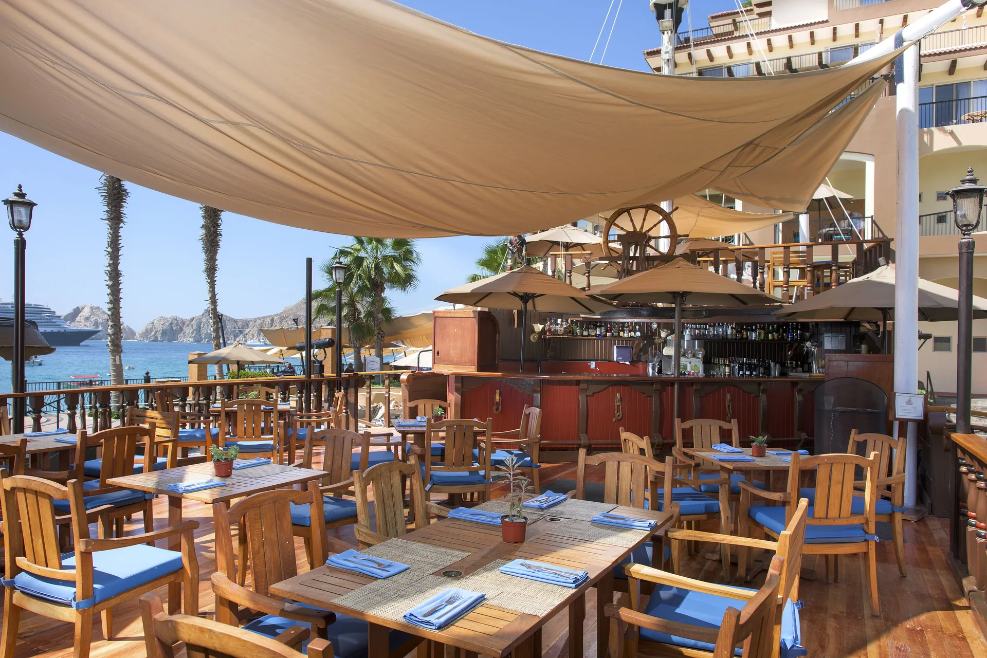 Outdoor bar deck at Villa del Arco Beach Resort & Spa Cabo San Lucas with wood tables, shade sails, and ocean views.
