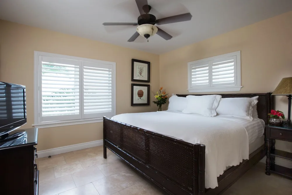 Bedroom with white shutters, dark wood bed, and TV at Villa del Mar.