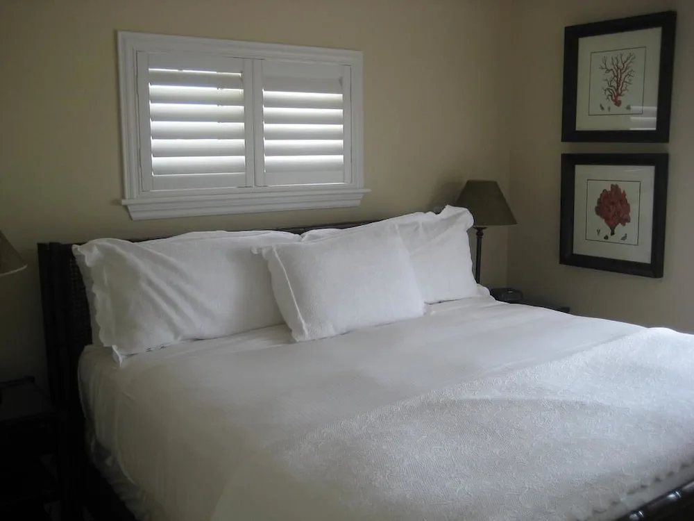 Bedroom with white bedding, shutters, bedside lamp, and coral artwork at Villa del Mar.