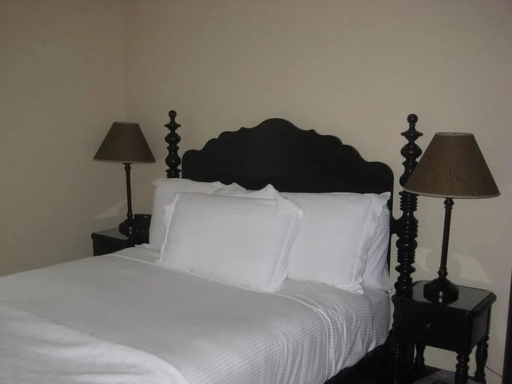 Guest room bed with white linens and dark wood posts at Villa del Mar.