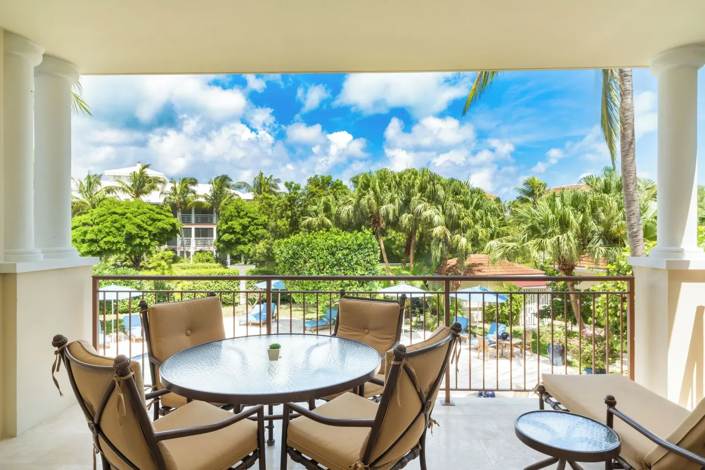 Luxury Suite balcony with dining set, lounge chair, palms, and pool view at Villa del Mar.