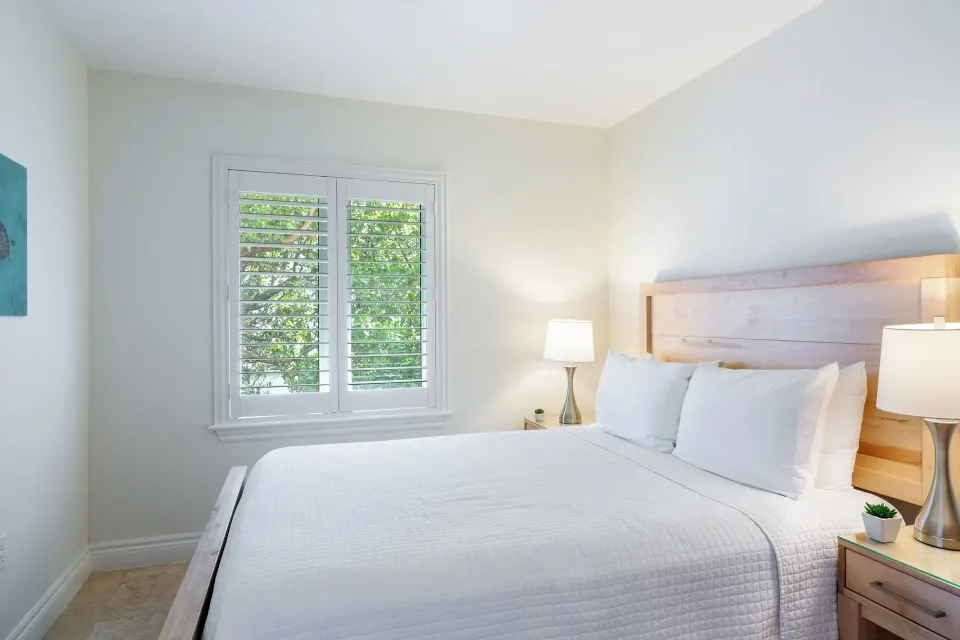 Luxury Suite two-bedroom guest room with a queen bed, bedside lamps, and shuttered window at Villa del Mar.