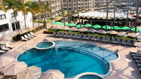 Curved pool with loungers and green umbrellas at Villa del Palmar Beach Resort and Spa, Puerto Vallarta.
