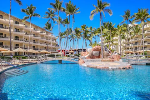 Palm-lined pool with bridge and rock feature at Villa del Palmar Beach Resort and Spa, Puerto Vallarta.
