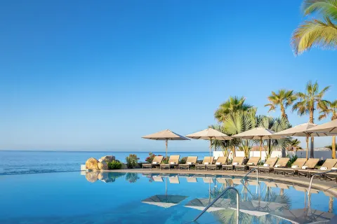 Curved infinity pool with umbrellas and ocean horizon at Villa La Valencia Los Cabos Beach Resort & Spa.