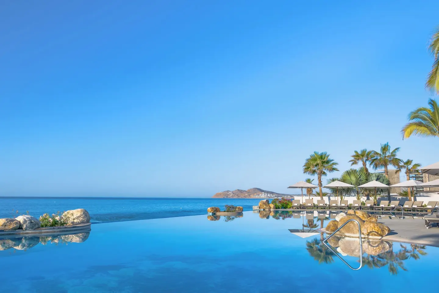 Infinity pool with ocean and distant coastline at Villa La Valencia Los Cabos Beach Resort & Spa.
