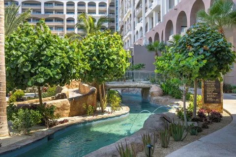 Landscaped lazy river with resort buildings at Villa La Valencia Los Cabos Beach Resort & Spa.
