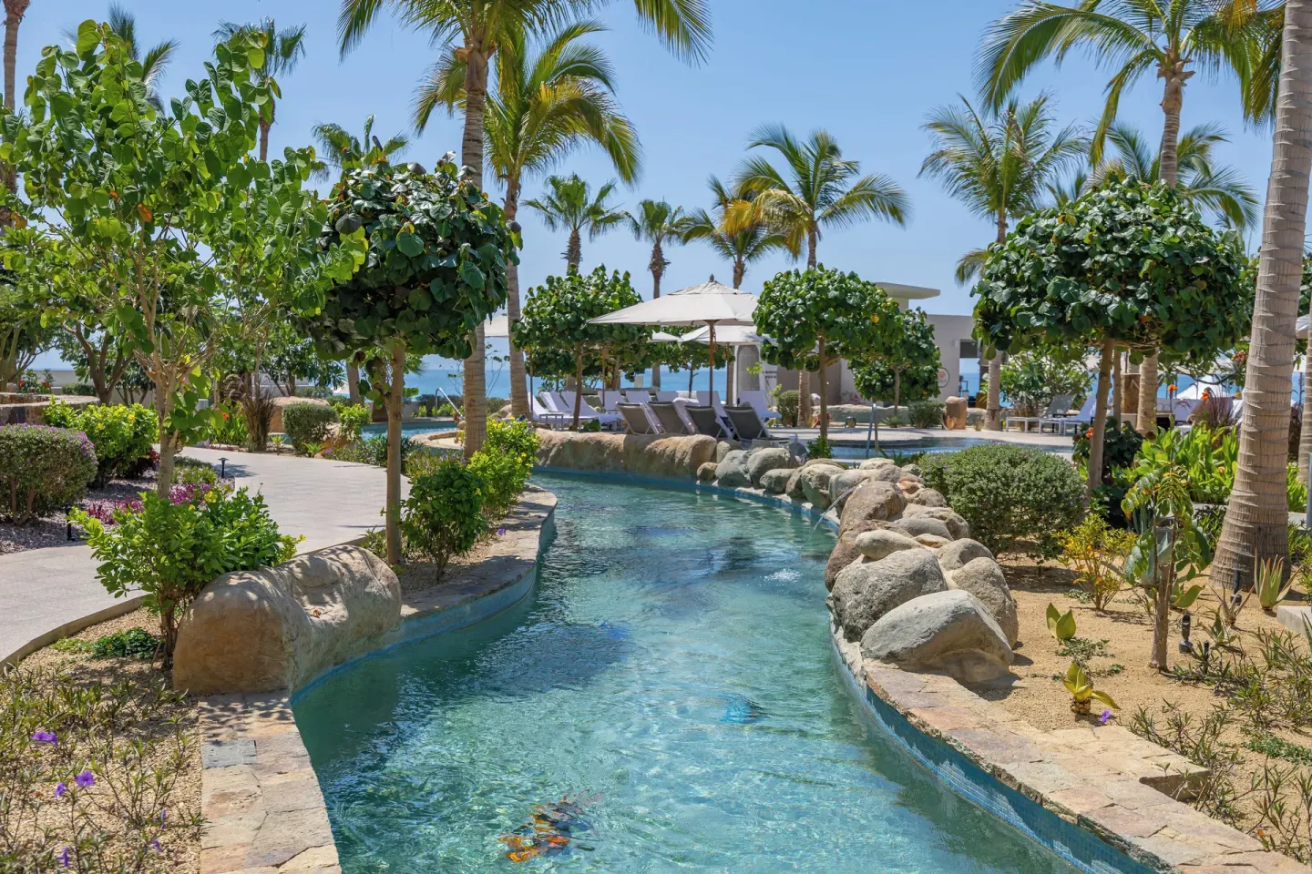 Lazy river curving toward ocean-facing loungers at Villa La Valencia Los Cabos Beach Resort & Spa.