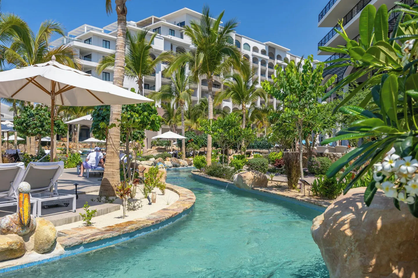 Lazy river beside palms, loungers, and resort buildings at Villa La Valencia Los Cabos Beach Resort & Spa.