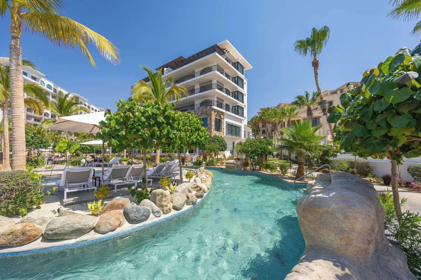 Lazy river with rock edging and palms at Villa La Valencia Los Cabos Beach Resort & Spa.
