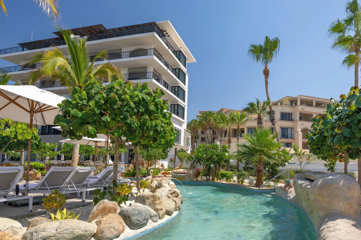 Lazy river with loungers and resort buildings at Villa La Valencia Los Cabos Beach Resort & Spa.