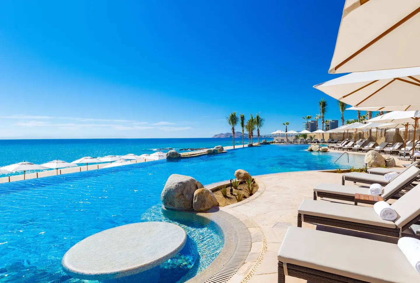 Infinity pool, ocean, loungers and umbrellas at Villa La Valencia Los Cabos Beach Resort & Spa.