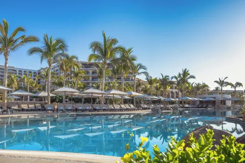 Palm-lined pool with umbrellas and resort buildings at Villa La Valencia Los Cabos Beach Resort & Spa.