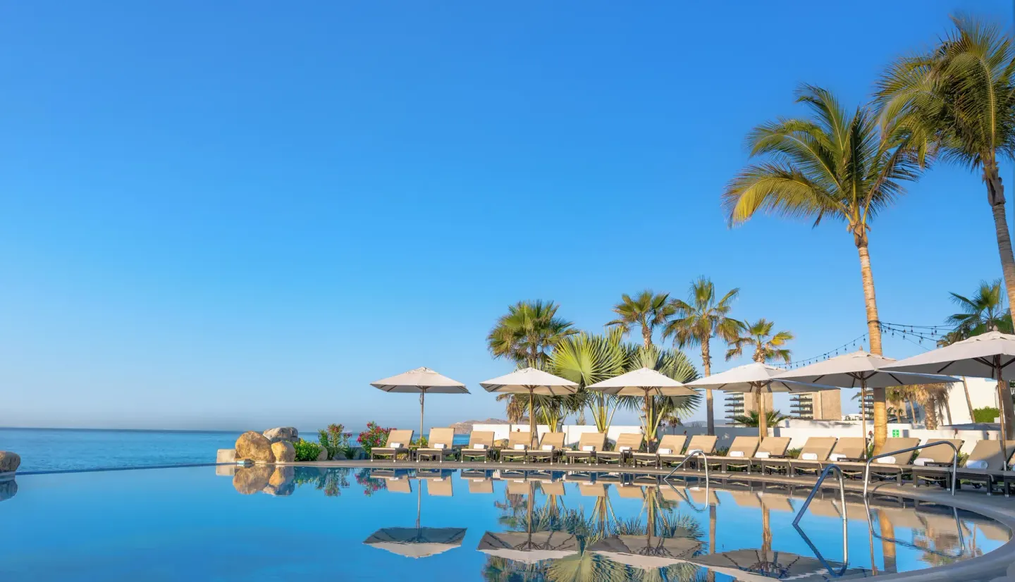 Pool terrace with umbrellas, palms, and sea views at Villa La Valencia Los Cabos Beach Resort & Spa.