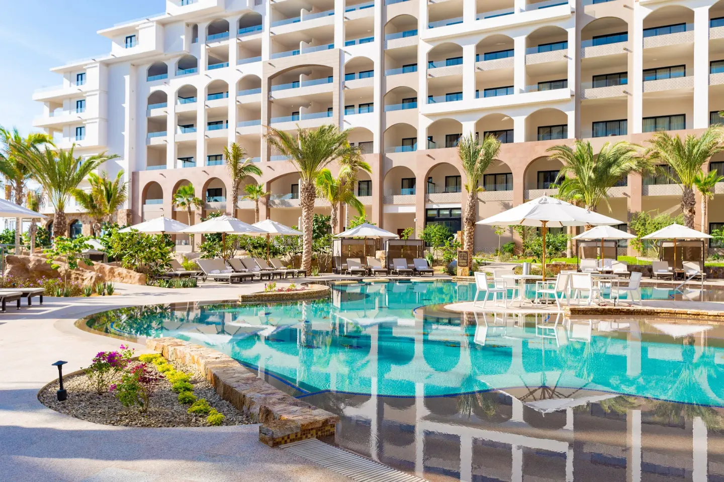 Pool terrace with umbrellas, loungers and arched balconies at Villa La Valencia Los Cabos Beach Resort & Spa.