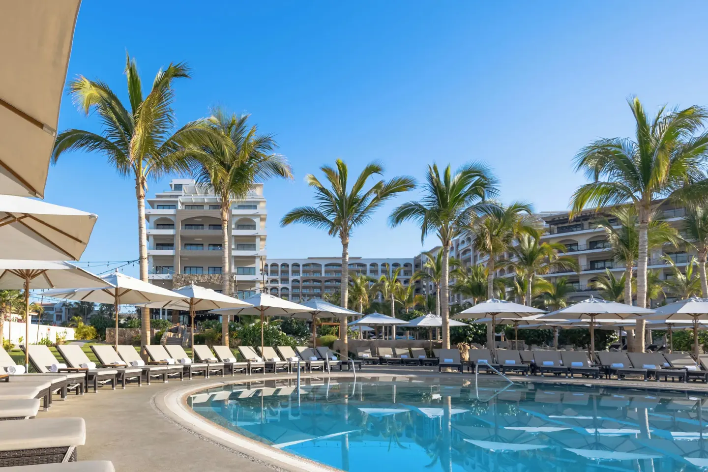 Resort pool with palms, umbrellas, and guest room buildings at Villa La Valencia Los Cabos Beach Resort & Spa.