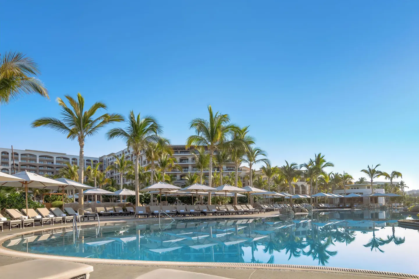 Wide pool view with palms, umbrellas, and resort buildings at Villa La Valencia Los Cabos Beach Resort & Spa.