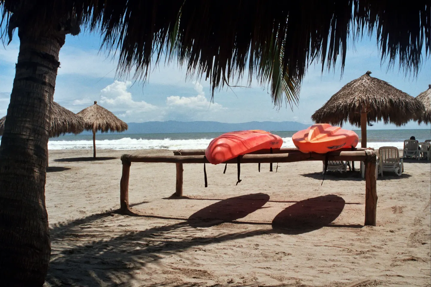 Kayaks rest on a beach rack between palapas and ocean waves at Villa Varadero.