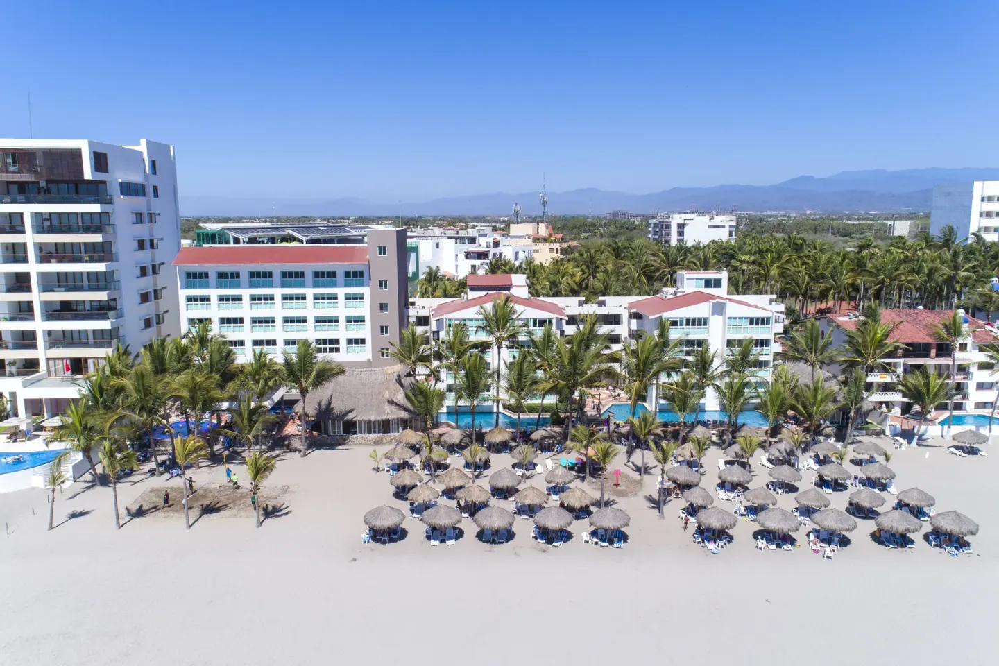 Aerial view of the beachfront, pools, palms, and palapa shade at Villa Varadero.