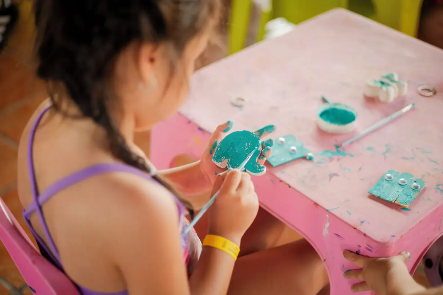A child paints a small craft shape at a pink activity table at Villa Varadero.