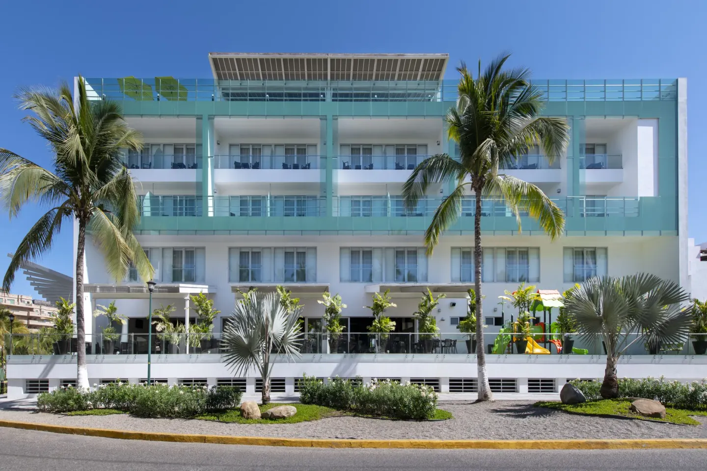 The white and turquoise exterior of Villa Varadero stands behind palms and landscaping.