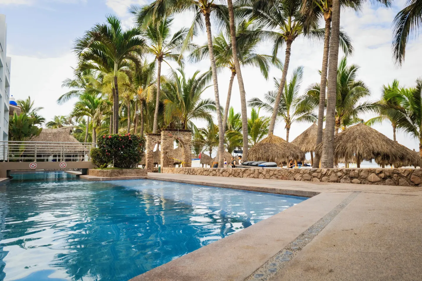 Palm-lined outdoor pool beside palapa shade structures at Villa Varadero.